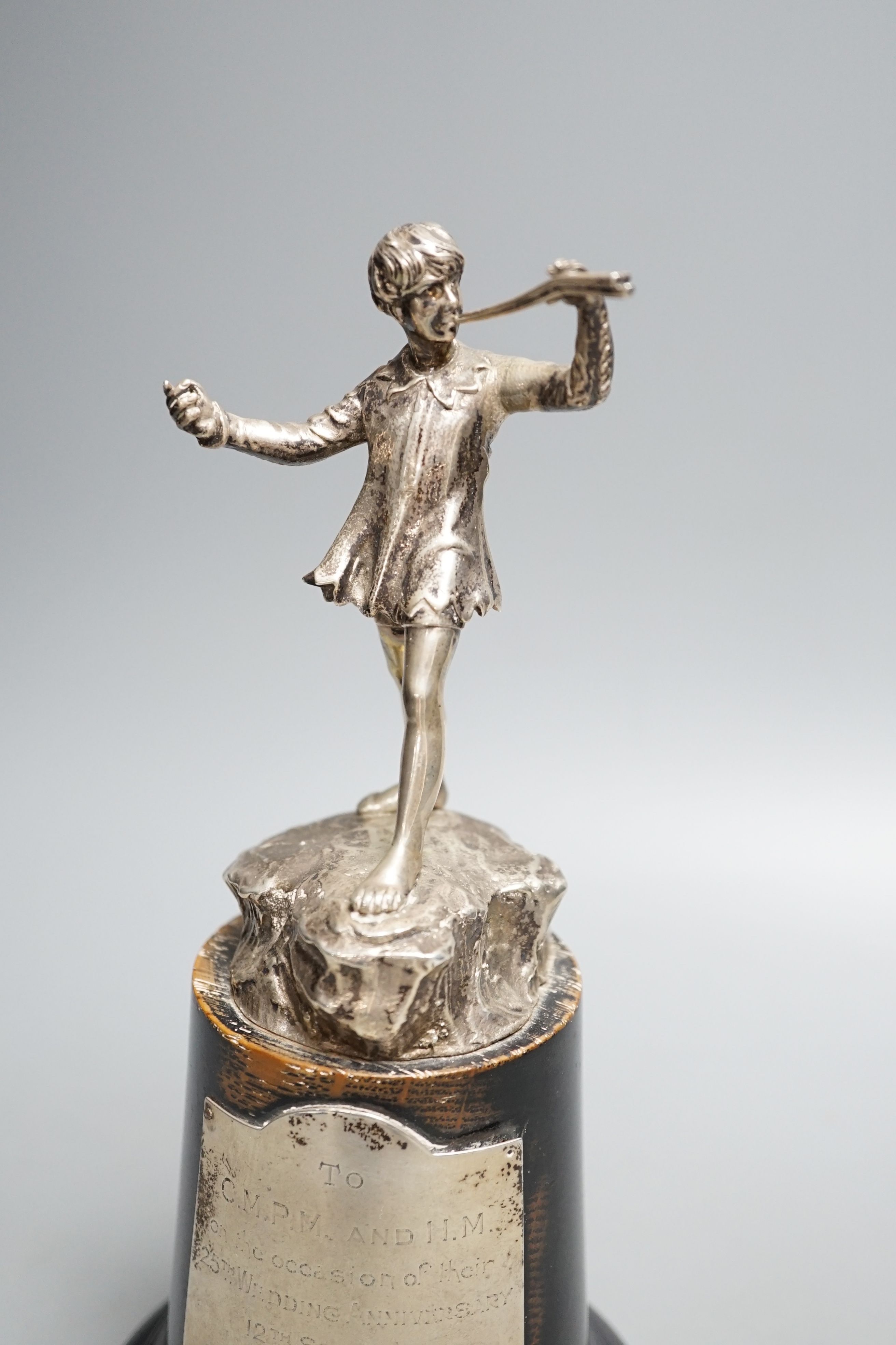 A late 1940's silver presentation figure of a young boy playing the pipes, on a rocky base, Goldsmiths & Silversmiths Co Ltd, London, 1949, on a wooden plinth with engraved presentation plaque, overall height 23.5cm